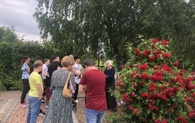 Uczestnicy zabawy stoją przy wielkim krzewie kwitnących na czerwono r&oacute;ż