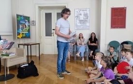 Kilka dzieci siedzi na spotkaniu na podłodze przed nimi autor.