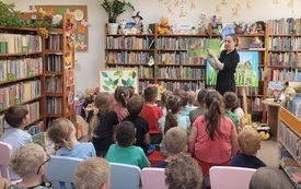 Bibliotekarka prezentuje siedzącym dzieciom książkę z obrazkami