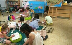 Grupa dzieci rysuje siedząc na podłodze w bibliotece