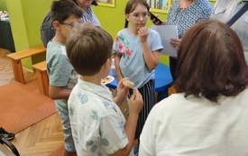 Dzieci i dorośli rozmawiają stojąc i jedząc ciastka