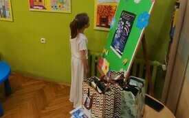 Dziewczynka stoi przed ścianą z wystawą prac konkursowych