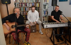 Trzech mężczyzn daje koncert grając na gitarze, keyboardzie i kahonie