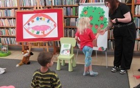Dziecko stoi przy tablicy, na kt&oacute;rej widać drzewo i truskawki