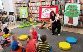 Młoda bibliotekarka czyta siedzącym na podłodze dzieciom
