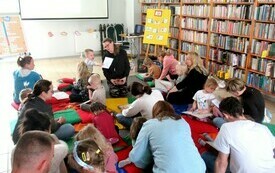 Dzieci wraz z rodzicami siedzą na podłodze w bibliotece