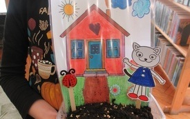 Dziewczynka trzymające w ręku pudełko z ziemią i obrazkiem domku.