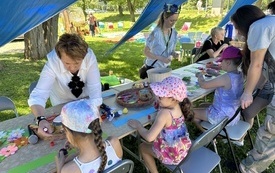 Warsztaty plastyczne plenerowe. Dzieci przy stolikach tworzące prace z papieru.