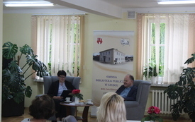 Bibliotekarka z Ks. Kazimierz Sowa siedzą na fotelach i rozmawiają. 