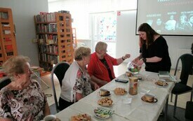 Bibliotekarka trzyma pojemnik z losami, czytelniczki wybierają los.