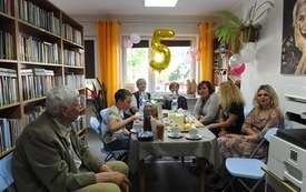 Grupa ludzi siedzi przy stole, w tle balon z cyfrą 5.
