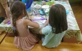 Dwie dziewczynki siedzą tyłem, wykonują prace plastyczne z papieru. 