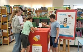 Grupa dzieci wrzuca kartki do urny w akcji - wybory książkowe.