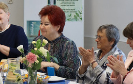 Kilka kobiet siedzi przy stole, klaszczą.