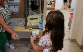 Maszyna z popcornem, dziewczynka trzyma pudełeczko wypełnione popcornem. 