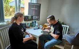 Autor podpisuje książkę, obok siedzi kobieta.