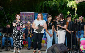 Dyrektor biblioteki - kobieta we wzorzystej sukience przemawia na scenie, obok prowadzące spotkanie oraz chór.