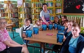 Grupa młodych ludzi trzyma książki Barbary Kosmowskiej, W tle regały biblioteczne.