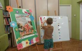 Dziecko stoi przy planszy i przykleja papier.