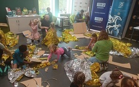 Dzieci z rodzicami podczas warsztatów. Tworzą zbroje z koców termicznych i tektury.