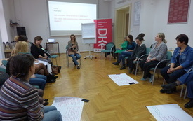 Bibliotekarki siedzą w kręgu, prowadząca tłumaczy, w tle logo DKK.