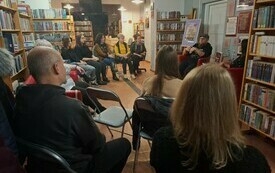 W przestrzeni bibliotecznej zgromadzona publiczność na spotkaniu autorskim.