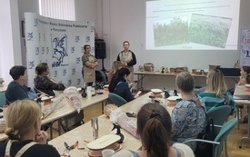 W sali przy dużych stołach siedzą uczestnicy warsztat&oacute;w. 