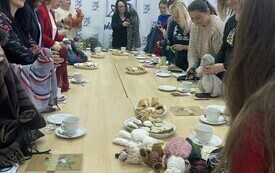 Grupa bibliotekarzy stoi przy długim stole i trzyma w rękach marionetki z materiał&oacute;w. 