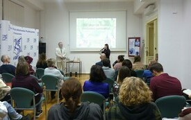 Grono os&oacute;b podczas słuchania wykładu. Bibliotekarka wita gościa. 