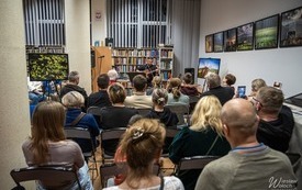 Publiczność we wnętrzu biblioteki podczas występu muzycznego. 