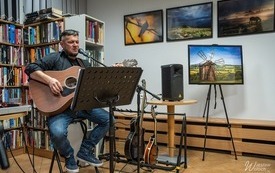 Mężczyzna z gitarą na wysokim krześle podczas występu.