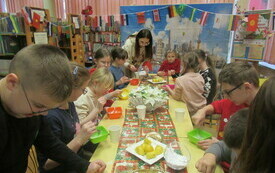 Przy stole bibliotekarka wraz z dziećmi tworzy lukier w miseczkach.