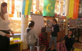 Dzieci rozwiązują ćwiczenia na tablicy. U góry rozwieszone flagi.