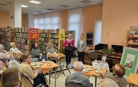 Grupa os&oacute;b siedzi przy stolikach w sali bibliotecznej