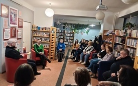 Grupa os&oacute;b w r&oacute;żnym wieku siedzi w sali bibliotecznej