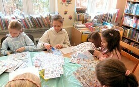 Grupa dzieci siedzi przy stole z arkuszami naklejek