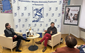 Pisarz gestykuluje podczas rozmowy z bibliotekarką. 