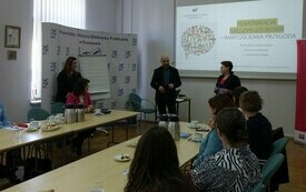 Widok sali szkoleniowej i prowadzącego, kt&oacute;ry stoi przy ekranie z prezentacją