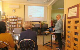 Kobieta stoi w bibliotece i omawia prezentację multimedialną.