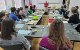 Uczestnicy warsztatów siedzą przy stole zwróceni w kierunku prowadzącego spotkanie starszego mężczyzny.