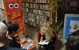 Młoda kobieta w blond włosach podczas podpisywania książki. Obok Grupa ludzi.