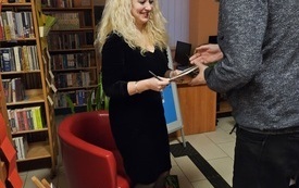 Młoda kobieta podaje książkę stojącemu obok mężczyźnie.