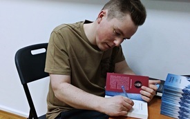 Młody mężczyzna podpisuje swoją książkę.