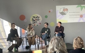 Cztery osoby siedzące na scenie przed zgromadzoną publicznością, w tle prezentacja multimedialna.