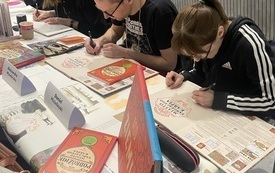 Grupa osób siedzących przy stole i piszących.