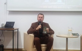 Mężczyzna siedzi w fotelu i trzyma w ręku mikrofon.