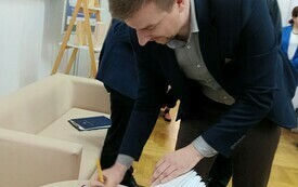 Mężczyzna w garniturze wpisujący się do kroniki bibliotecznej.