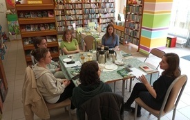 Młodzież siedząca przy stoliku w bibliotece, w tle regały z książkami.