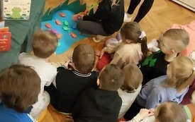 Dziewczynka podczas zabawy z żabkami. Obok grupa dzieci.