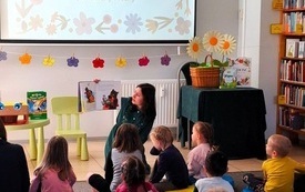 Kobieta siedzi na dywanie i pokazuje dzieciom ilustracje w książce